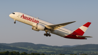 Lietadlo Boeing 787-9 Dreamliner spolocnosti Austrian Airlines v cerveno-bielej livereji strmo stupa do rannej oblohy po starte, zabery zo zeme zdola, v pozadi zelena rakuska krajina