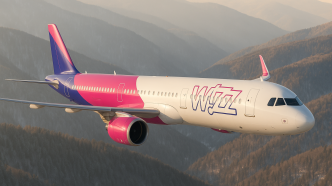 Airbus A321neo Wizz Air v livreji s bielou prednou časťou trupu, purpurovou zadnou časťou a fialovým chvostom za letu nad zalesnenými hrebeňmi v podvečernom svetle