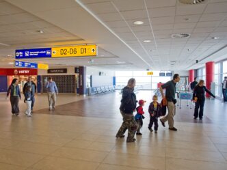 Presvetlená chodba terminálu so žltými smerovkami k východom D1 a D2, chodbou kráča niekoľko cestujúcich vrátane detí.