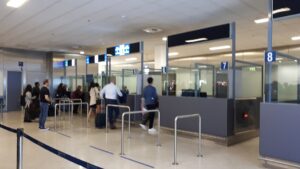Cestujúci prechádzajú pasovou kontrolou v hale letiska, pred kabínkami s pracovníkmi hraničnej kontroly
