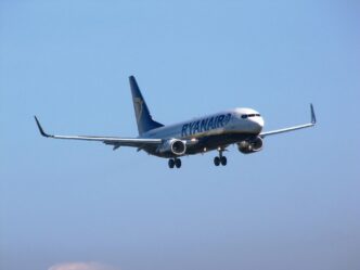 Modro-žlté lietadlo Boeing 737 spoločnosti Ryanair s vysunutým podvozkom krátko pred dosadnutím, v pozadí jasná obloha.