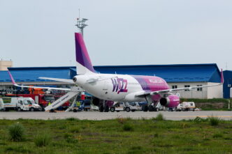 Bielo-purpurové lietadlo Wizz Air stojí na odbavovacej ploche s pristavenými nástupnými schodmi, okolo neho pozemná technika.