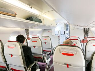 Kabína Austrian Airlines Embraer 195 počas nastupovania: sedadlá v červeno-čiernom poťahu a odkladací priestor nad hlavami
