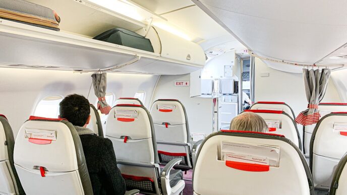 Kabína Austrian Airlines Embraer 195 počas nastupovania: sedadlá v červeno-čiernom poťahu a odkladací priestor nad hlavami