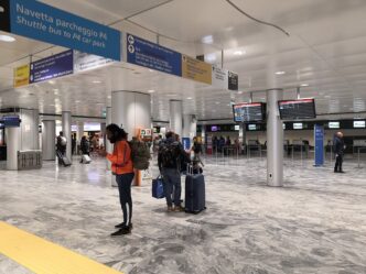 Svetlá odletová hala terminálu s cestujúcimi s kuframi, informačnými monitormi a smerovými tabuľami pod stropom