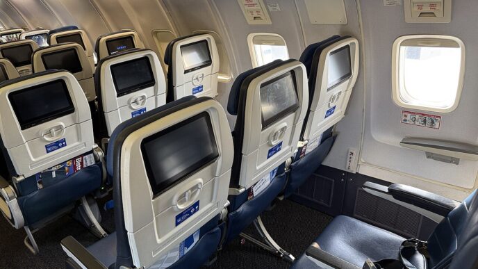 Kabína lietadla s radmi sedadiel pri dvoch núdzových východoch nad krídlom, pri oknách nálepky s pokynmi